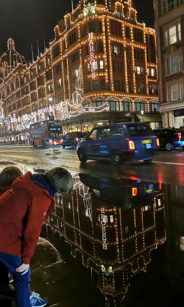 Kids looking in a puddle at the reflection of the Christmas lights on Harrods in London.