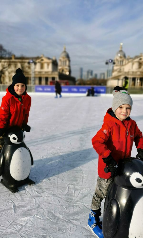 Two boys in red coats ice skating at Queens House - one of the best Christmas things to do for kids in London.