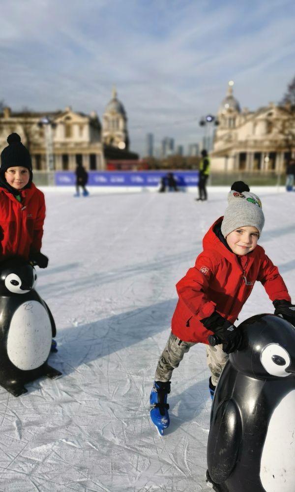 Two young boys in red jackets ice skating at the Queen's House Ice Rink in Greenwich - one of the best London ice rinks.