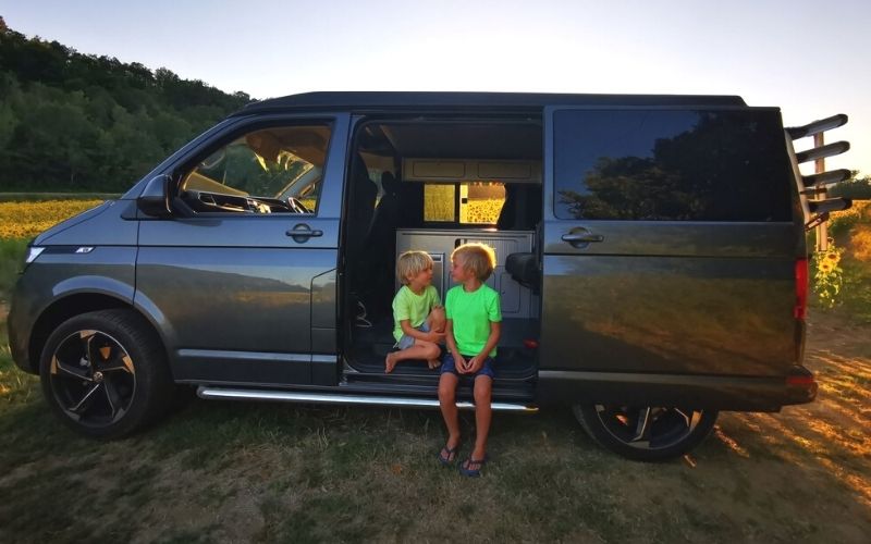 VW Campervan in a field of sunflowers at sunset.