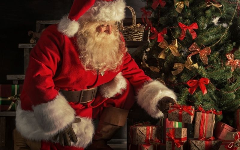 Santa placing presents under the Christmas tree.