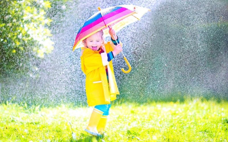 Toddler playing with a colourful umbrella in the rain.