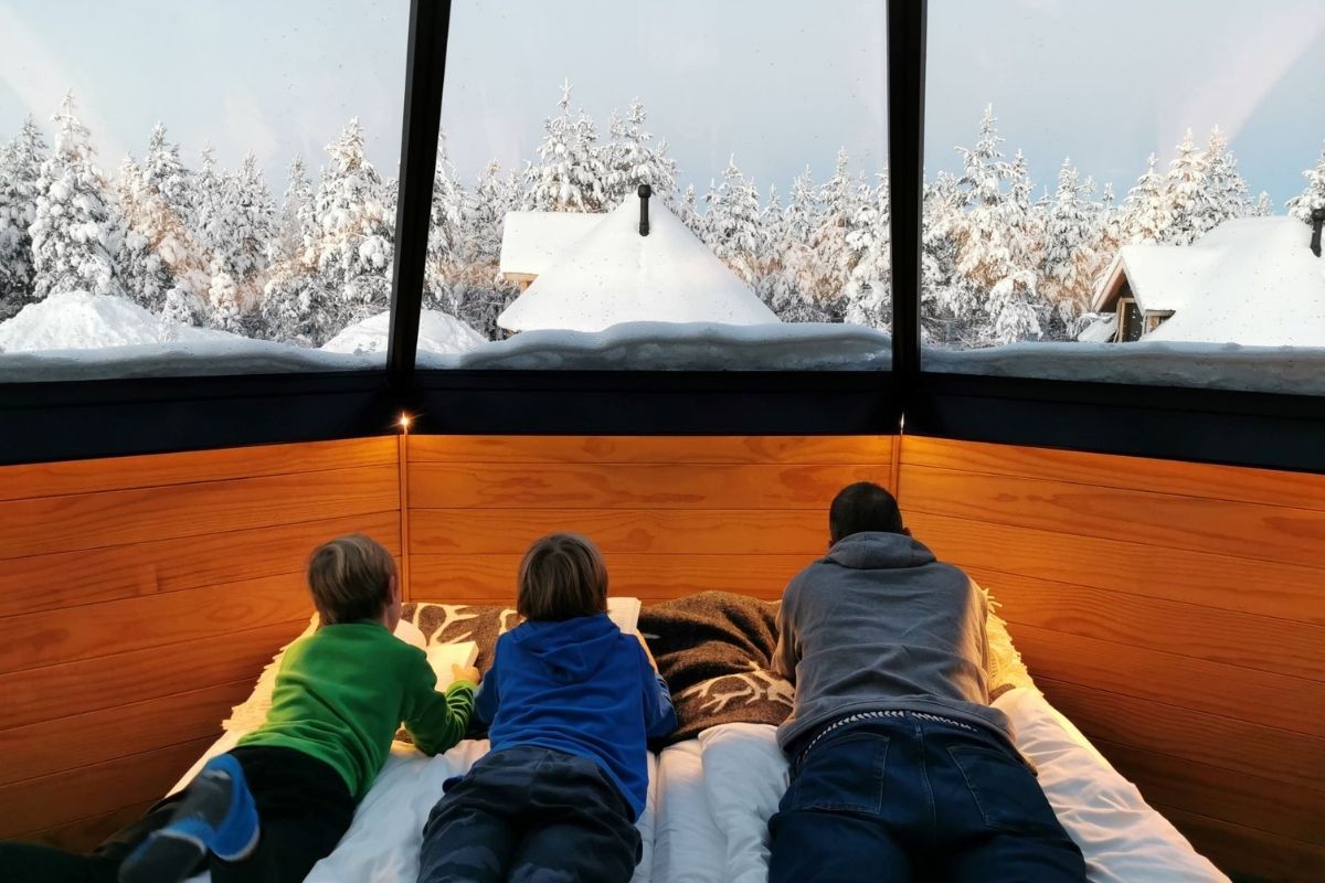 Family reading on a bed in a glass igloo in Lapland.