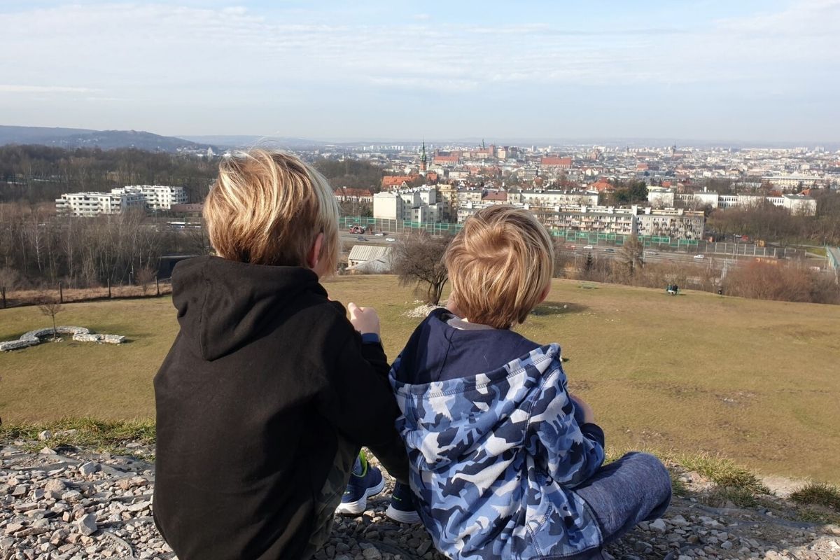Two kids sitting on top of Krakus Mound with a view of Krakow.