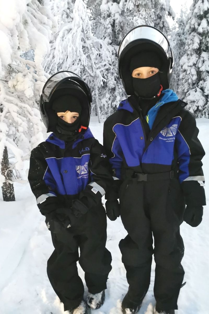 Two boys in snow gear with motorbike helmets ready to go snowmobiling in Lapland.