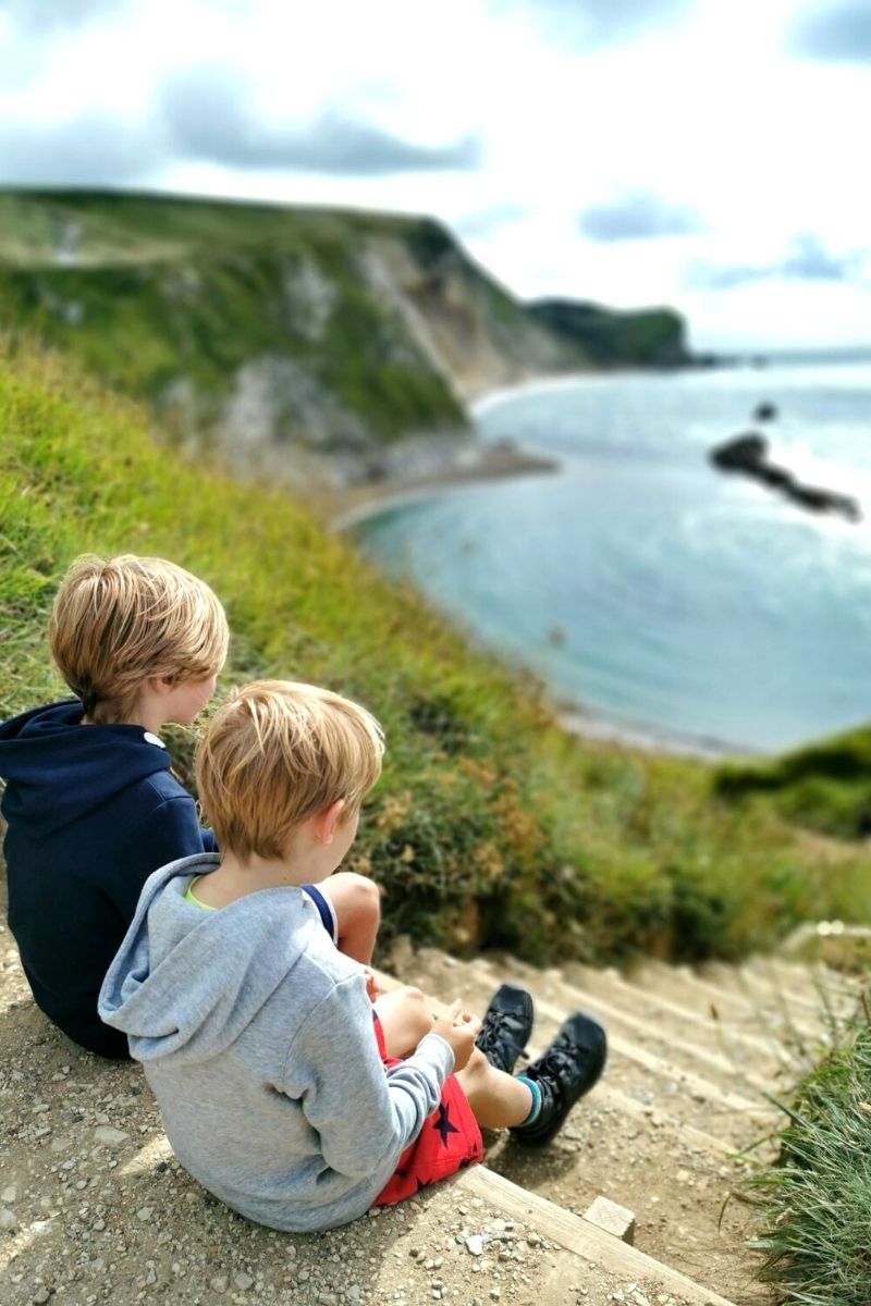 Two boys sitting at the top of the steps down to Man O War beach in Dorset.