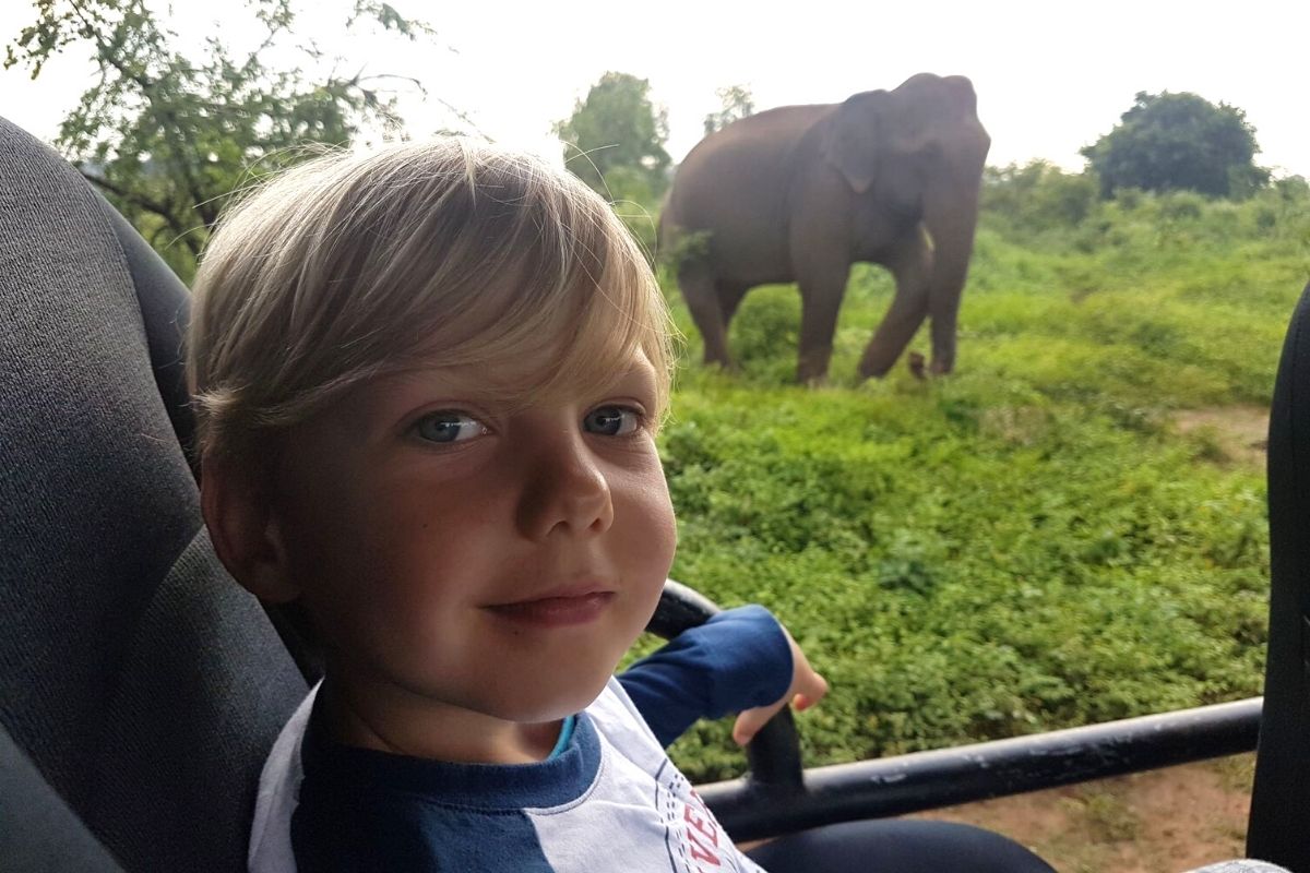 Young boy on a safari in Udawalawe National Park with an elephant in the background.