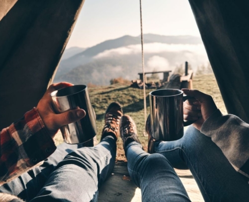 Couple enjoying view of mountain range from their tent with a cup of tea.