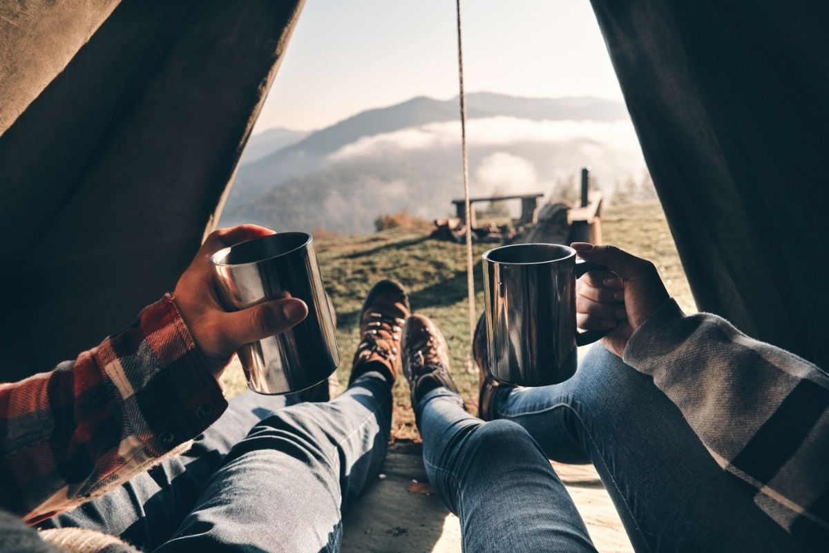 Couple enjoying view of mountain range from their tent with a cup of tea.