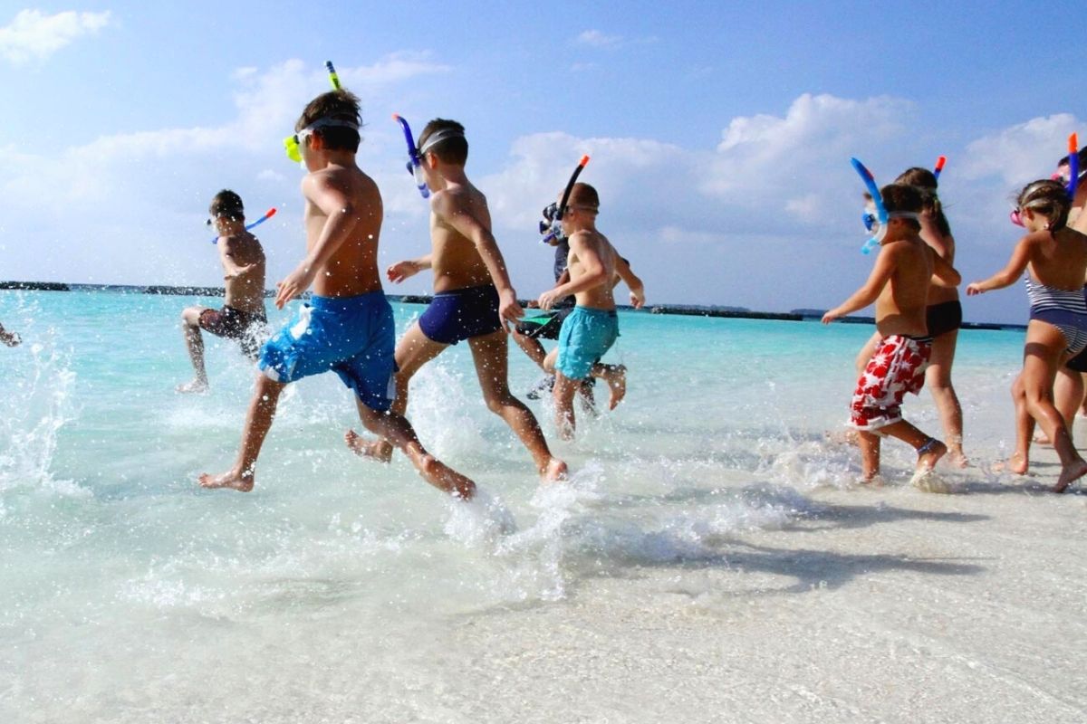 Kids running into the sea to go snorkeling in the Maldives at Kurumba.