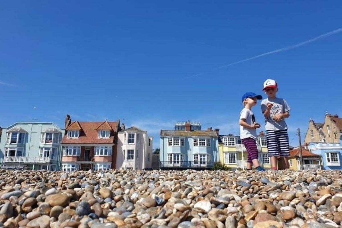 Two boys on the stony Aldeburgh Beach with colourful Victorian houses in the background.