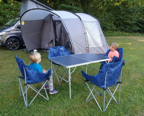 Two boys sitting in chairs on a campsite.