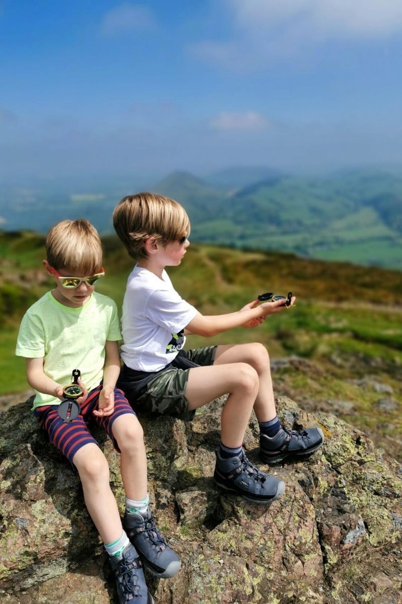 Two young boys sitting on top of a hill looking at their compasses.