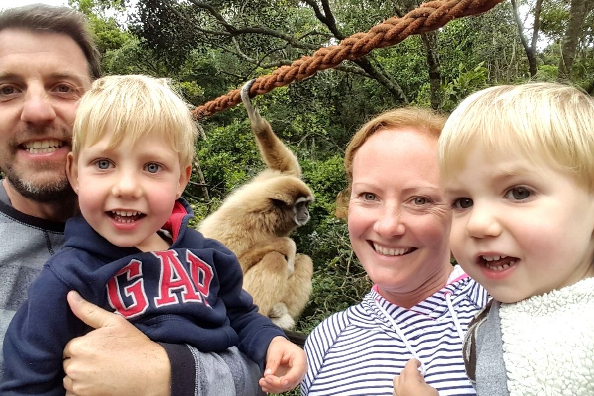 Family of four with 2 young boys with a monkey in the background.