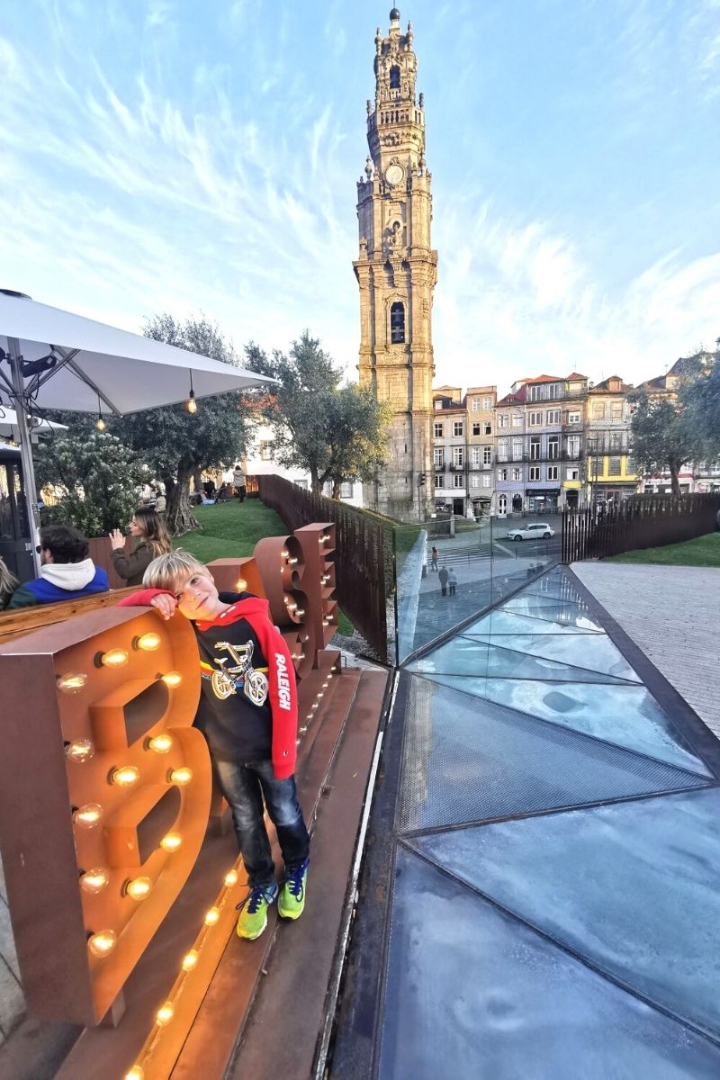 Small boy beside the sign of Base Porto in Porto with the Clerigos Tower in the background.