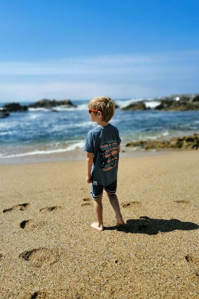 Small boy standing on Praia do Molhe beach in Porto.