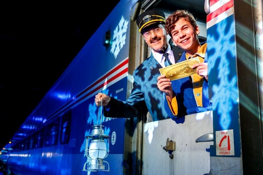 Boy holding Polar Express train ride ticket with conductor in background on board one of the Polar Express train rides in the US.