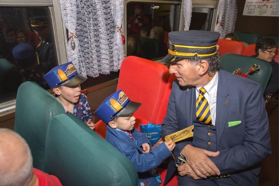 Conductor speaking to a little boy who is handing him his ticket on the Blackstone Valley Polar Express.