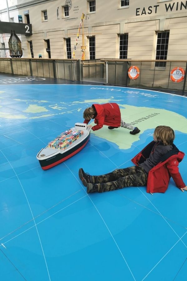 Kids pushing toy cargo ships around a map at the National Maritime Museum in London.