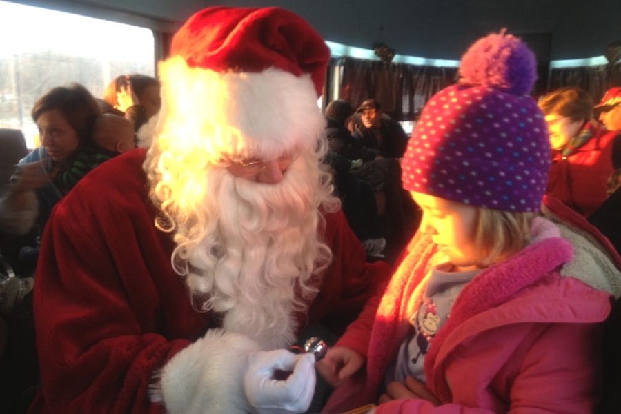 Santa presenting little girl in red bobble hat with a silver sleigh bell on the Polar Express train ride.