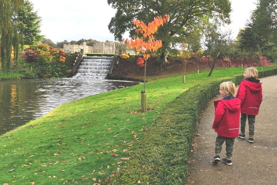 Two boys in red coats walking in the grounds of Leeds Castle in the autumn.