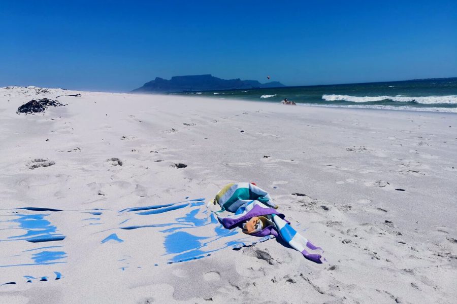 Dock and Bay towels covered in sand on Blaauwberg Nature Reserve in South Africa with Table Mountain in background.