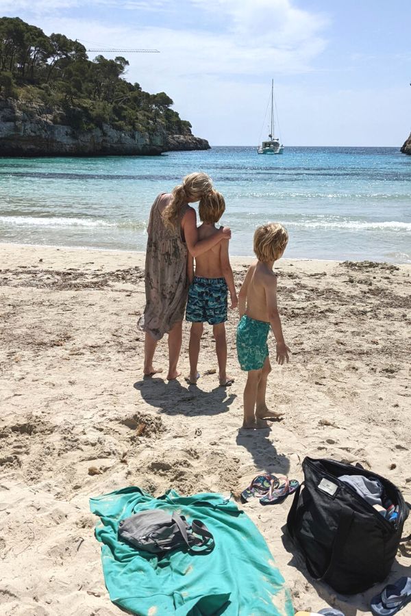 Mother and two boys on a beach looking out to a boat at sea.