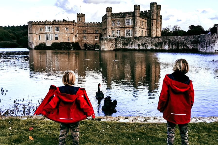 Two boys in red jackets with backs to camera looking across the moat to Leeds Castle in Kent.