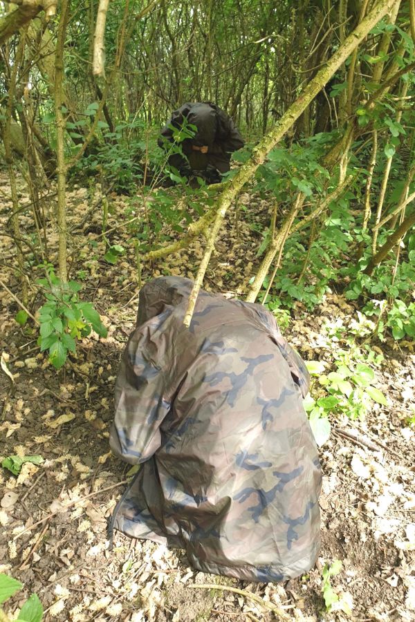 Two boys wearing TOG24 packable jackets in camouflage design hiding in the undergrowth.