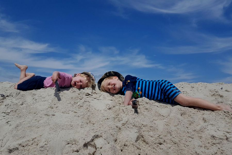 Two little boys lying in the sand at the beach.