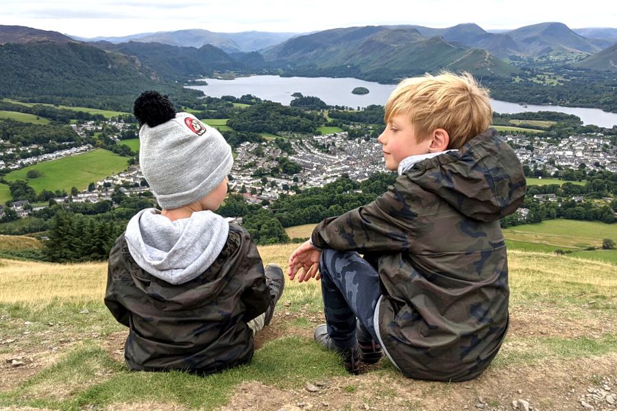 Two boys sitting on a hill overlooking a lake in the Lake District wearing TOG24 packable jackets.