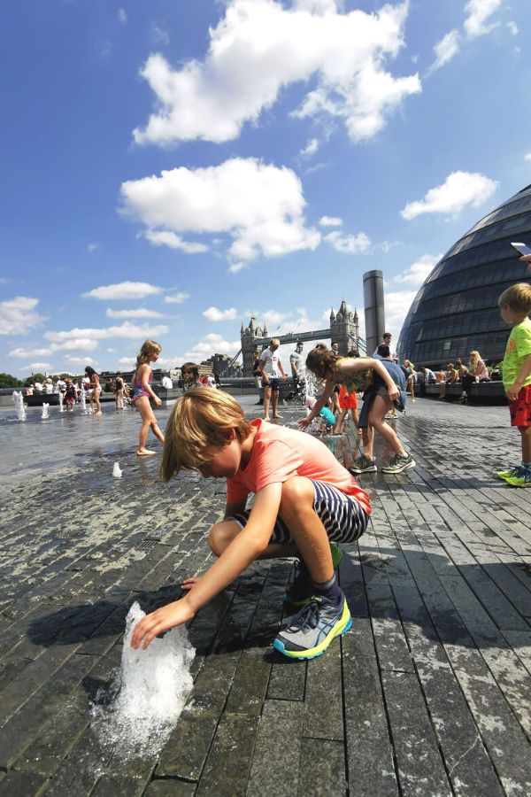 Boy playing in the splash pad at City Hall in London with Tower Bridge in the background.