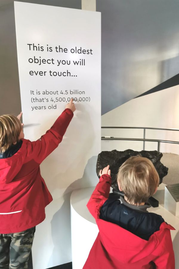 Two boys in red coats pointing to the oldest object at the Royal Observatory in Greenwich.
