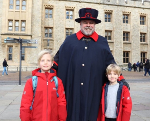 Two boys in red coats standing either side of a Yeoman at the Tower of London - one of the most visited attractions in London with kids.