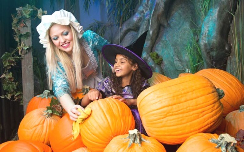 Lady and a young girl in Halloween costumes surrounded by pumpkins at Shrek's Adventure in London at Halloween.
