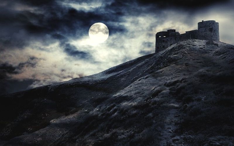 Silhouette of a castle in the moonlight with creepy clouds.