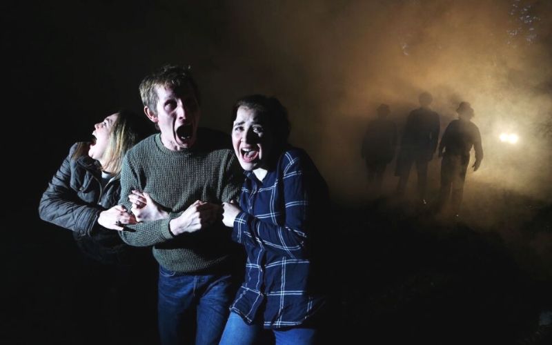 Three people huddled together screaming in the dark at Fright Night at Thorpe Park.