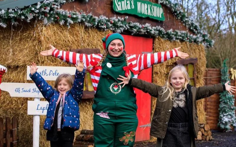 An Elf and two children outside Santa's Workshop at Bocketts Farm in Surrey at Christmas.
