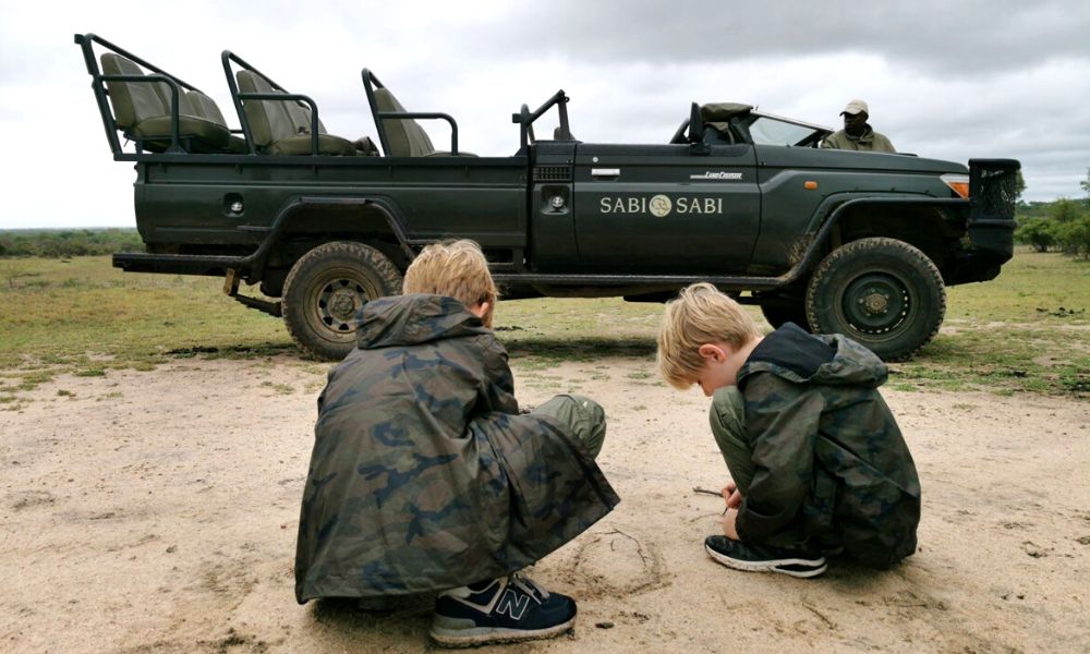 Kids looking at animal tracks on safari in the Kruger National Park.