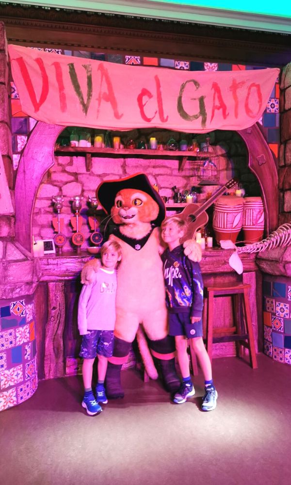 Two little boys posing with El Gato from Shrek's Adventure in London.