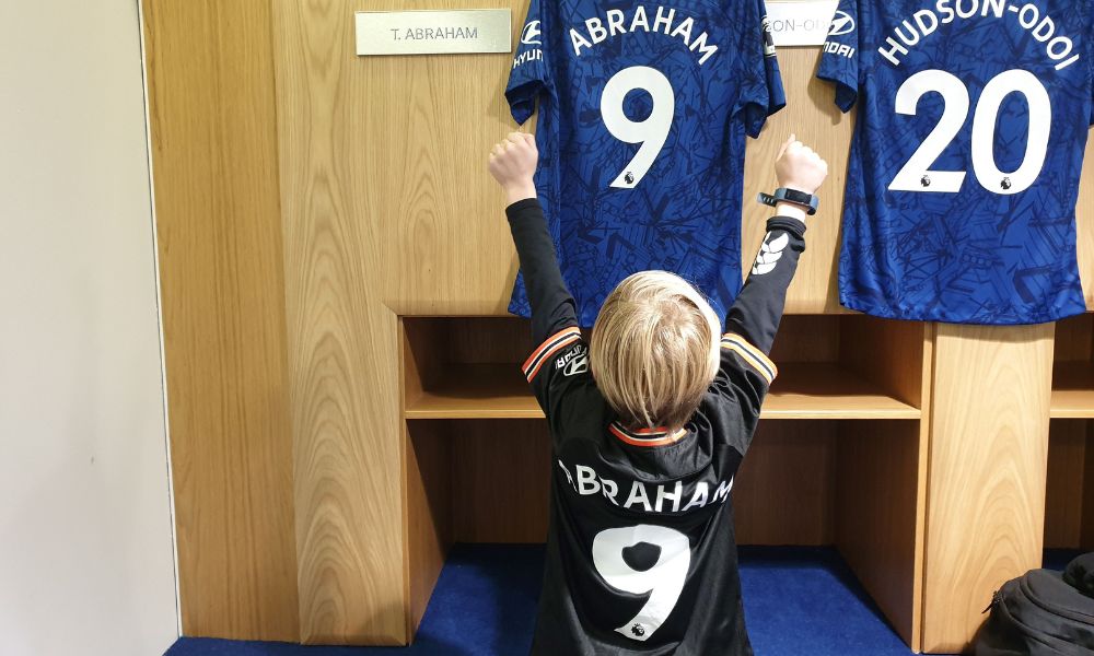 Little boy standing infront of a Tammy Abraham Chelsea jersey in the Chelsea FC changing rooms.