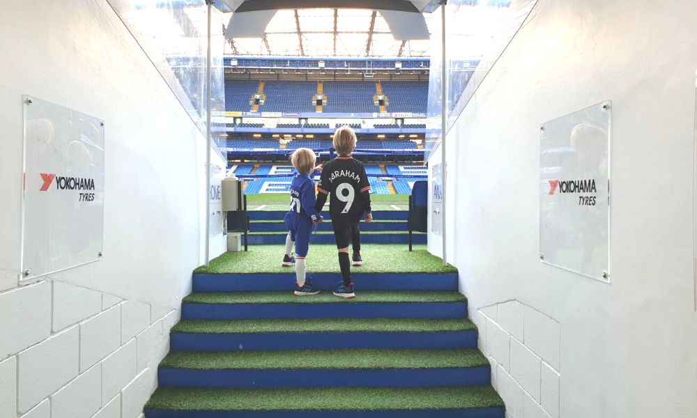 Two young boys walking out of the players' tunnel at Chelsea FC Stadium.