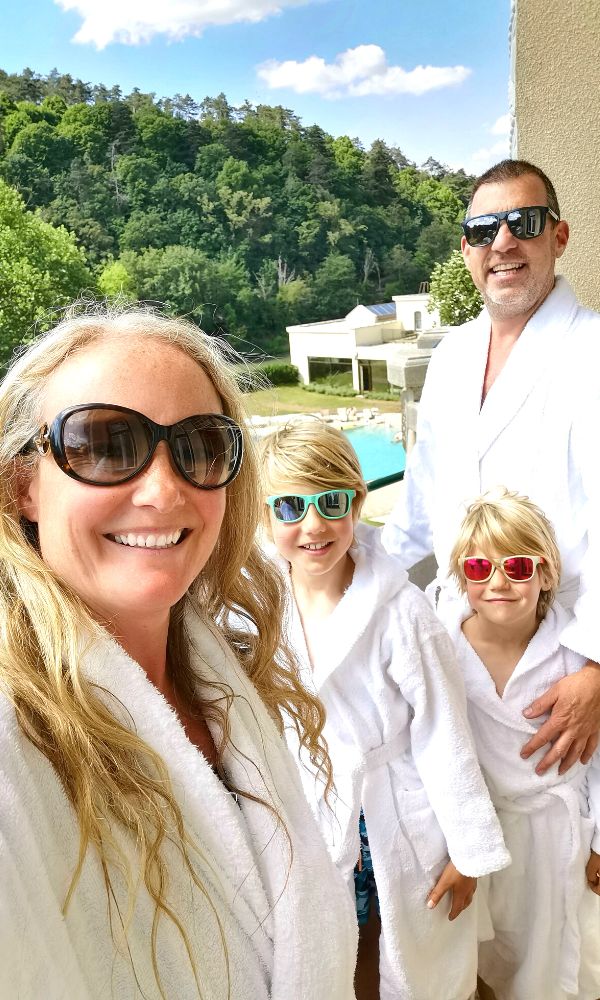 Family of four in bathrobes and sunglasses on a balcony at the Thermia Palace spa resort in Slovakia.