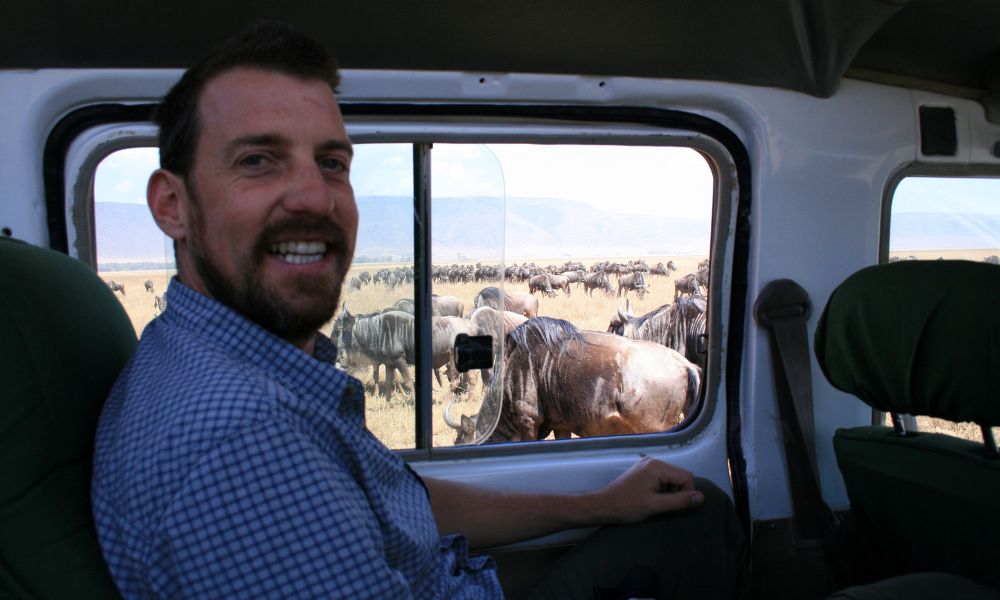 Man in a safari jeep surrounded by a herd of Wildebeest in the Serengeti National Park in Tanzania.