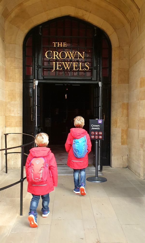 Two kids in red jackets with backpacks entering into the Crown Jewels exhibition at the Tower of London.