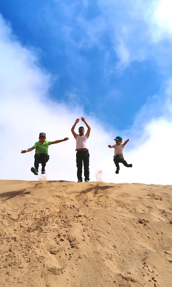 Family of three jumping off the top of a sand dune during a Swakopmund tour of the desert.