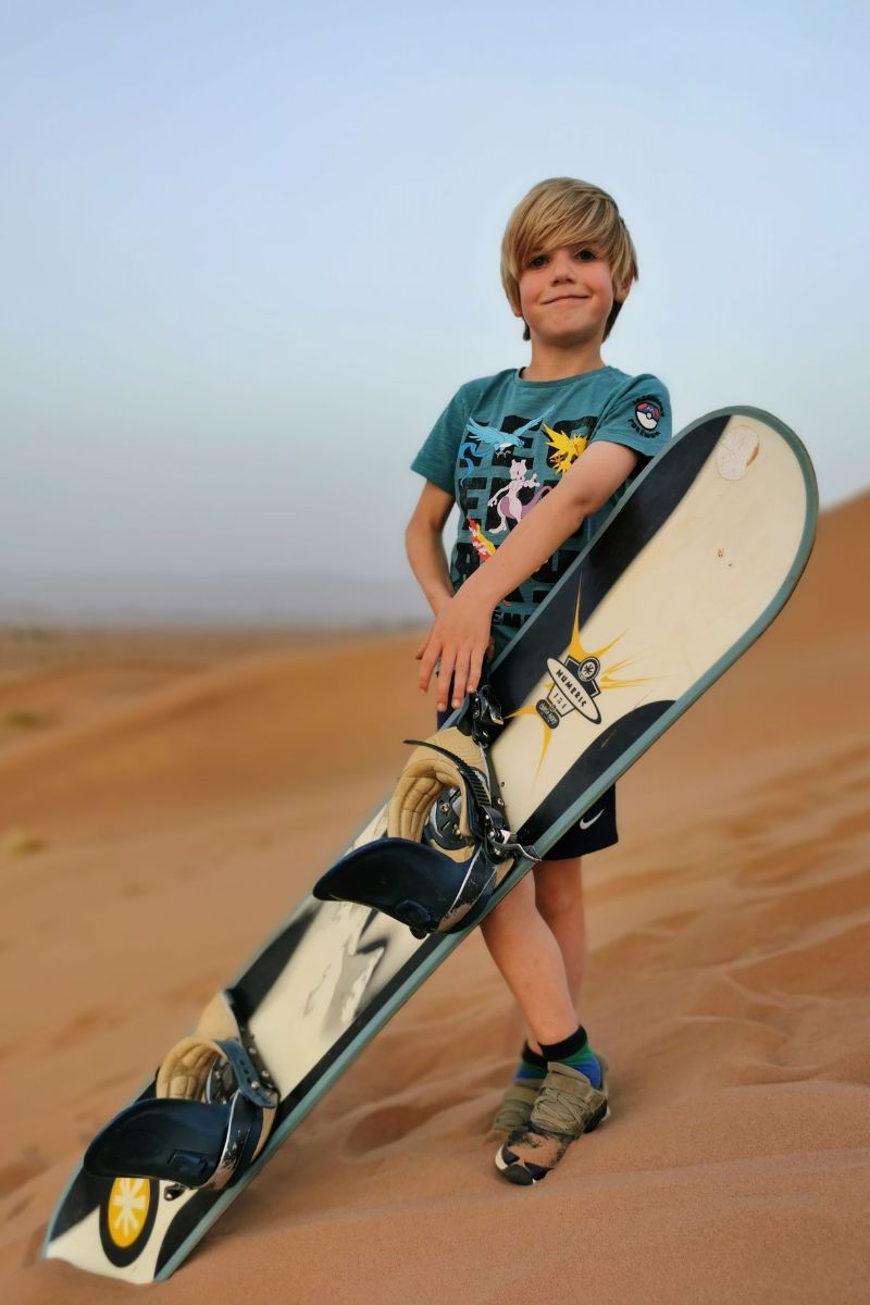 Child holding a snowboard on a sand dune in Tinfou in Morocco.