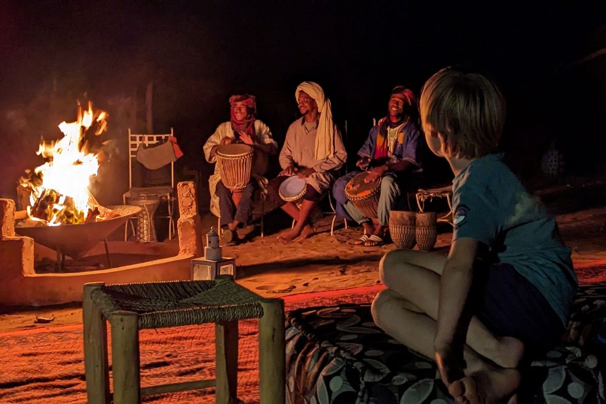 Child sitting by a camp fire in a Berber camp listening to traditional Berber music in Tinfou Desert Camp in Morocco.