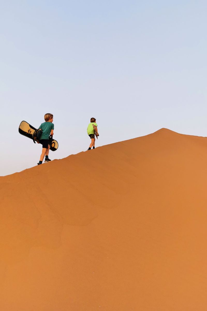Kids walking up a sand dune with snowboards to go sandboarding in Zagora.