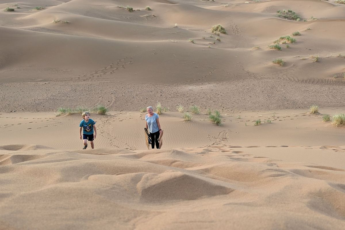 Mother and son carry snowboards up a sand dune in Zagora in Morocco.